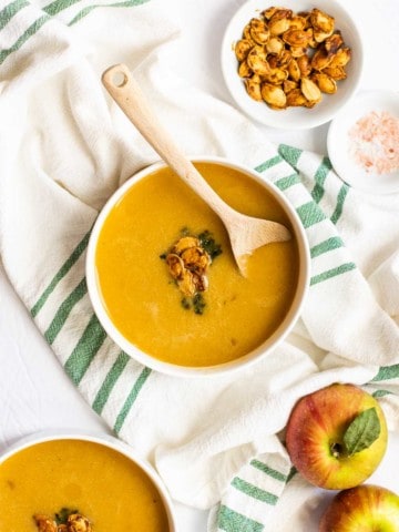 overhead shot of butternut squash soup in white bowl with wooden spoon and white and green napkin