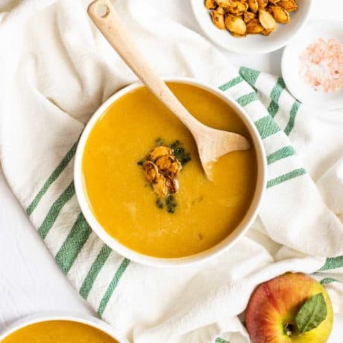 overhead shot of butternut squash soup in white bowl with wooden spoon and white and green napkin