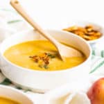 up close shot of yellow butternut squash soup with down spoon and pumpkin seeds on top
