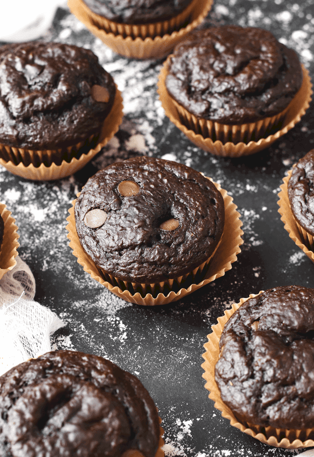 Up close shot of chocolate banana muffins in brown liners on a black background.