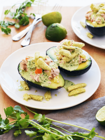 Two tuna stuffed avocados on a white plat with cilantro and limes in background