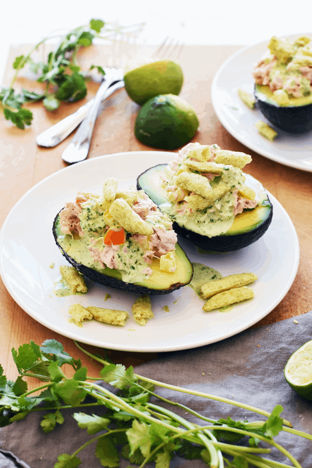 Two tuna stuffed avocados on a white plat with cilantro and limes in background