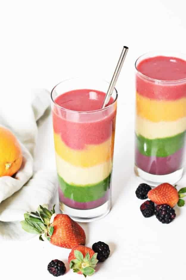 Rainbow layered smoothie in glass with straw and strawberries in foreground