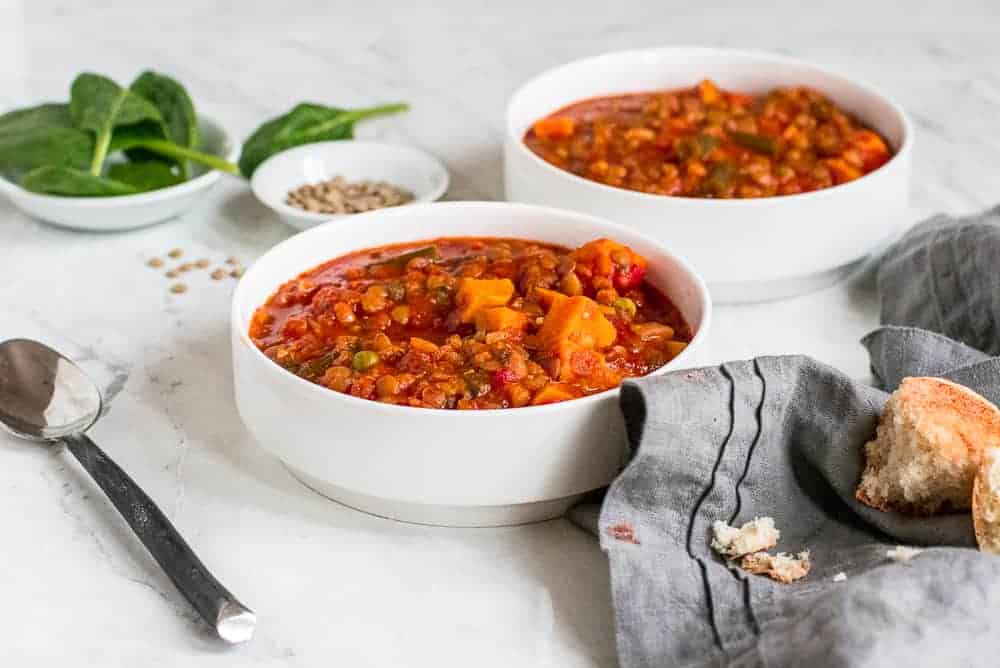 Two white bowls of Instant Pot vegetable soup with gray towel and spoon