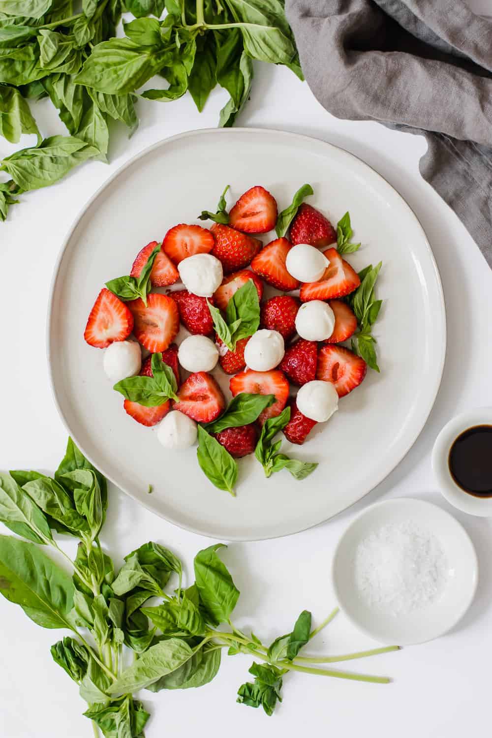 Overhead shot of strawberries, basil, and mozzarella on white plate with basil leaves around.