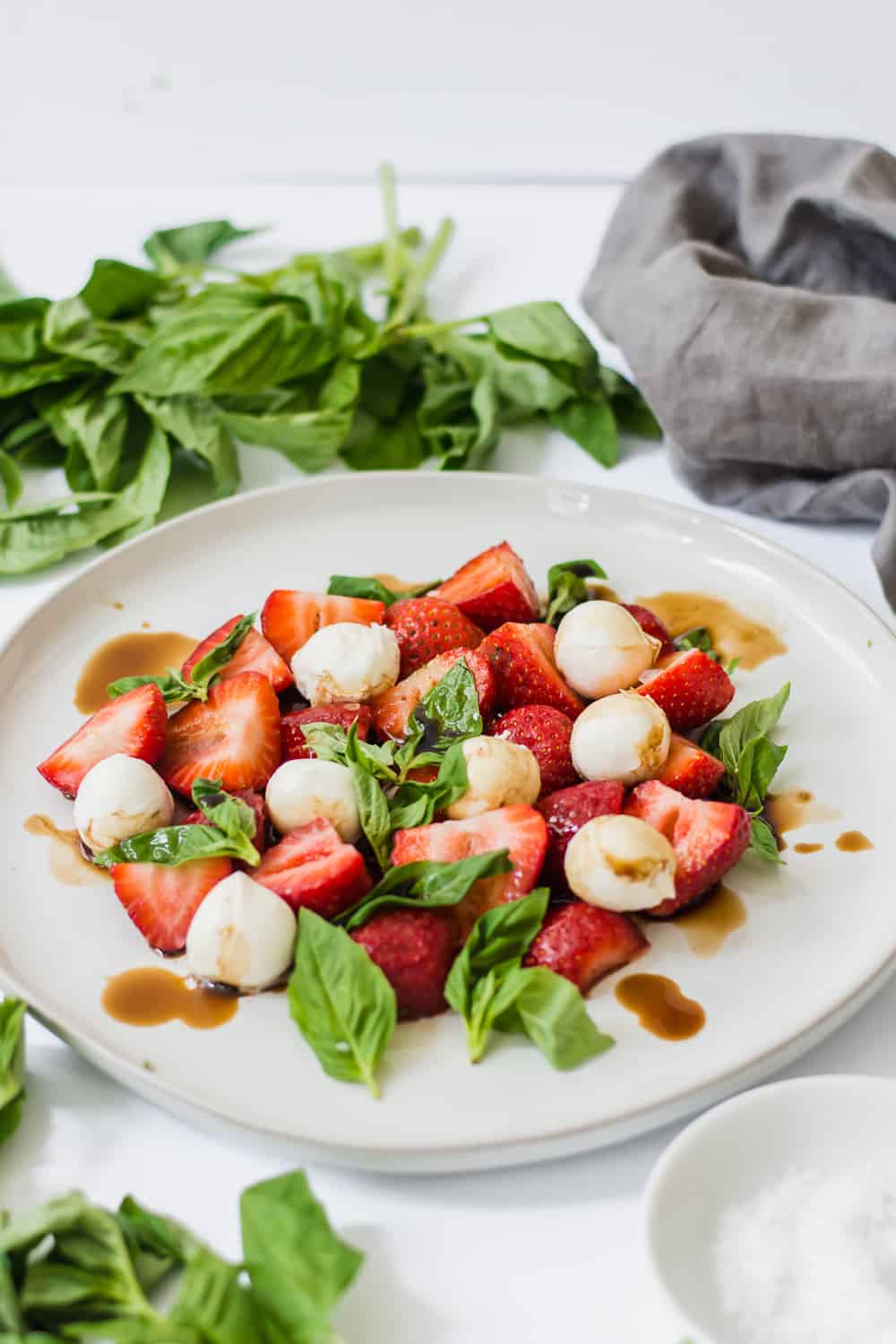 Close up pull back shot of white plate with strawberries, mozzarella balls, and basil leaves.