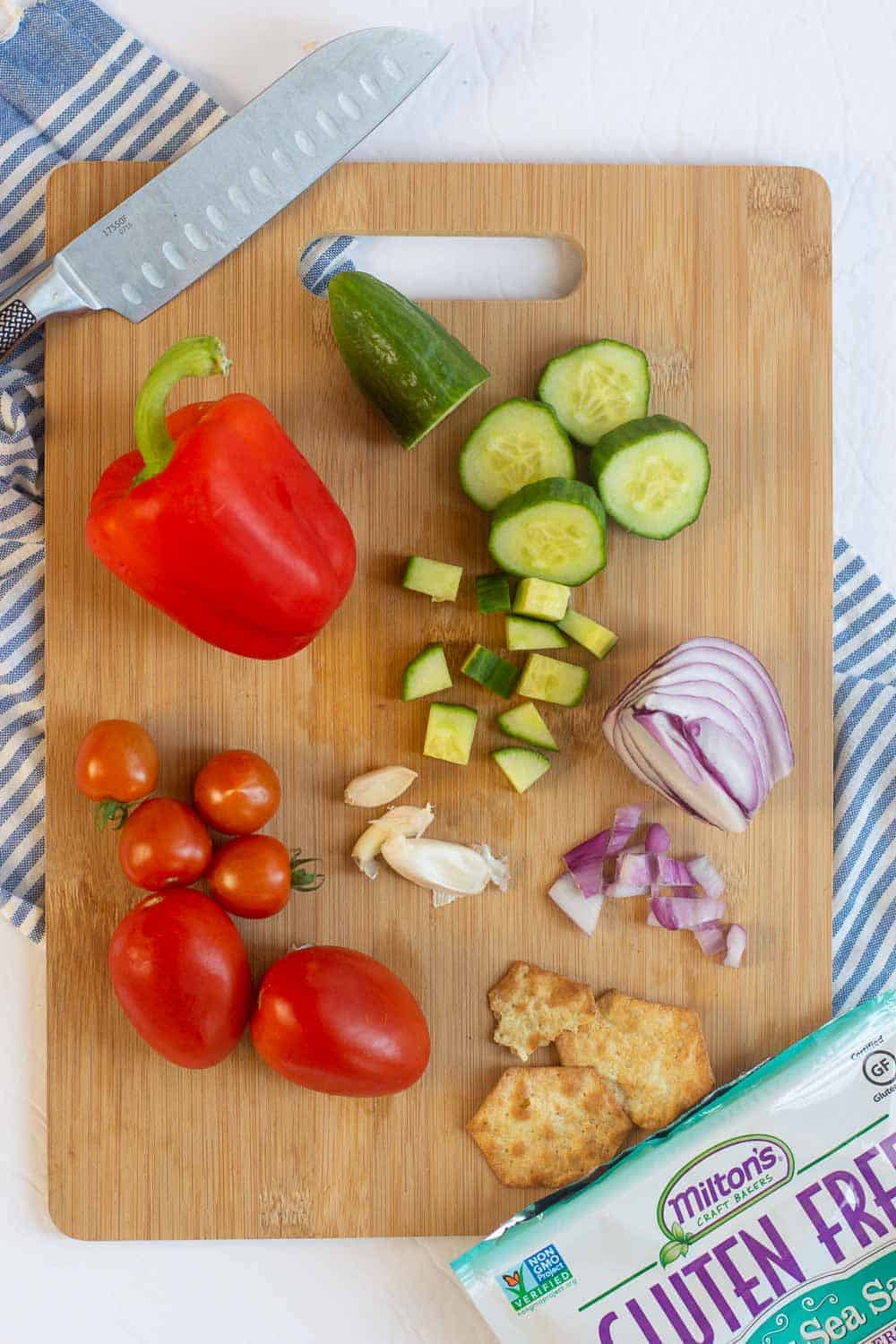 Wooden cutting board with tomatoes, red pepper, cucumber, red onion and crackers
