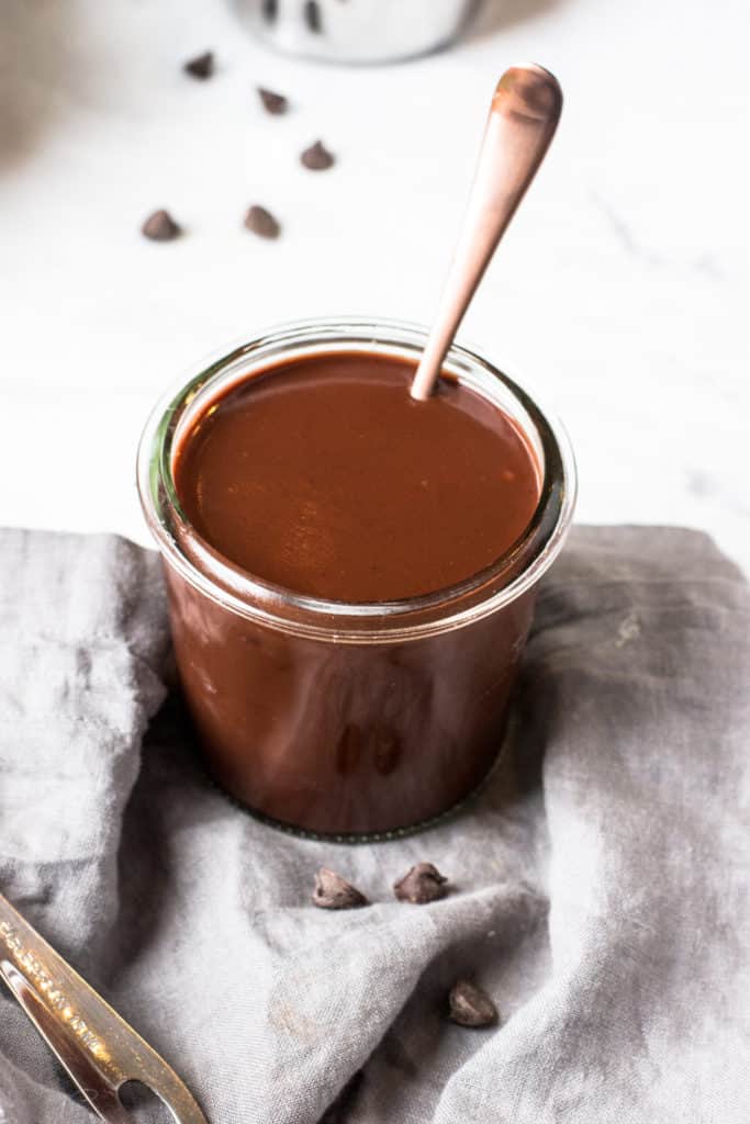 Up close shot of homemade chocolate sauce in glass jar with copper spoon