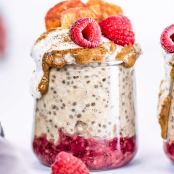 Big glass jar with overnight oats, red jam, and raspberries