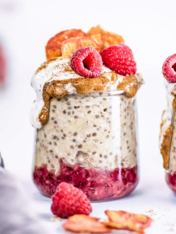 Big glass jar with overnight oats, red jam, and raspberries