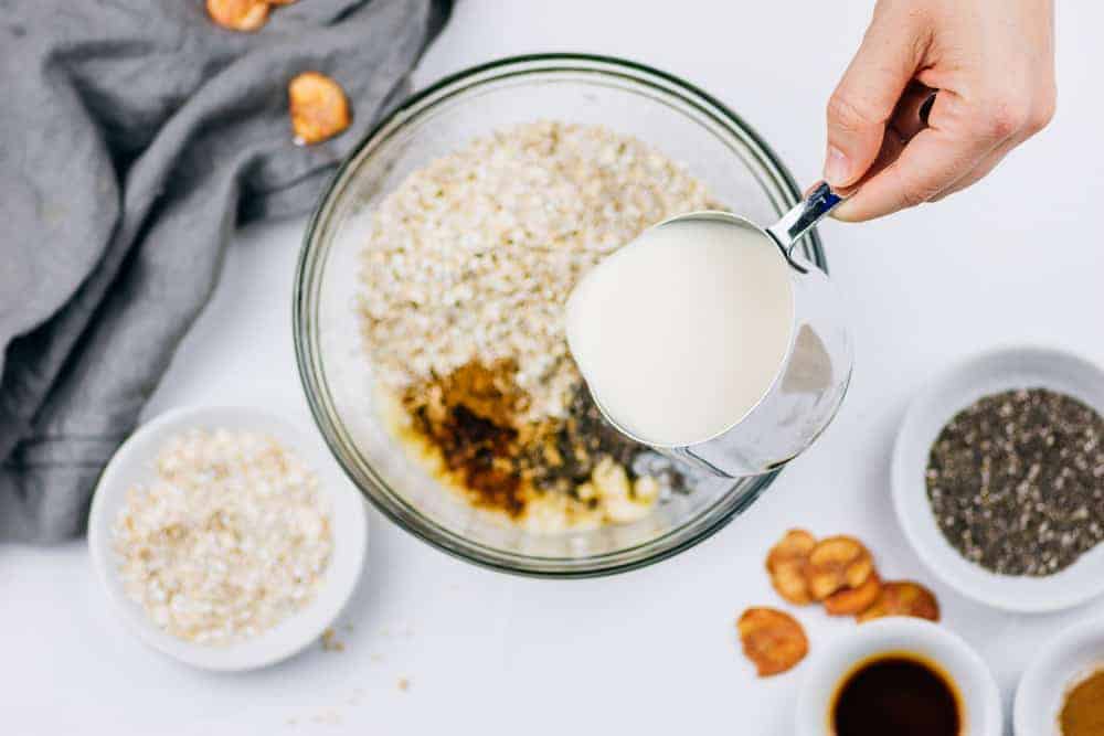 Overhead shot pouring milk into glass bowl with oats
