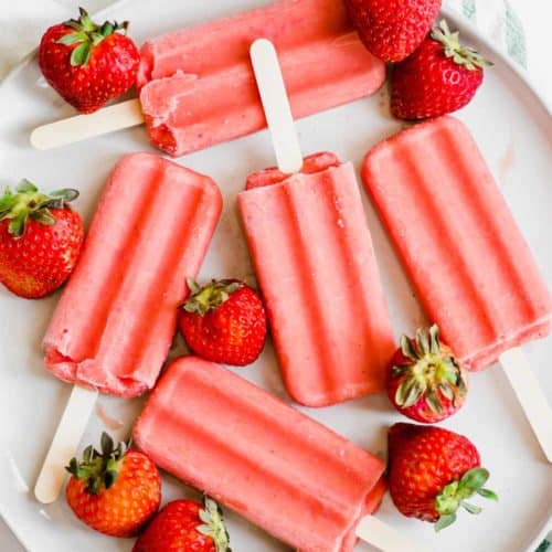 Overhead shot of strawberry popsicles on great plate with strawberries around it