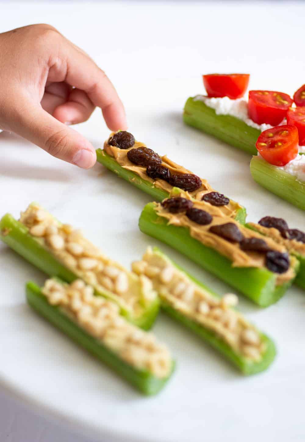 Pull back image of small hand grabbing celery with peanut butter and raisins