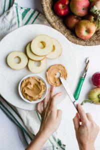 hands spreading peanut butter on sliced apples
