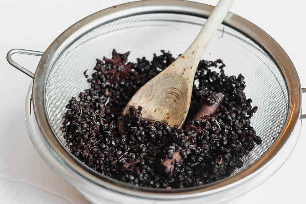 Strained elderberries and herbs in sieve with wooden spoon