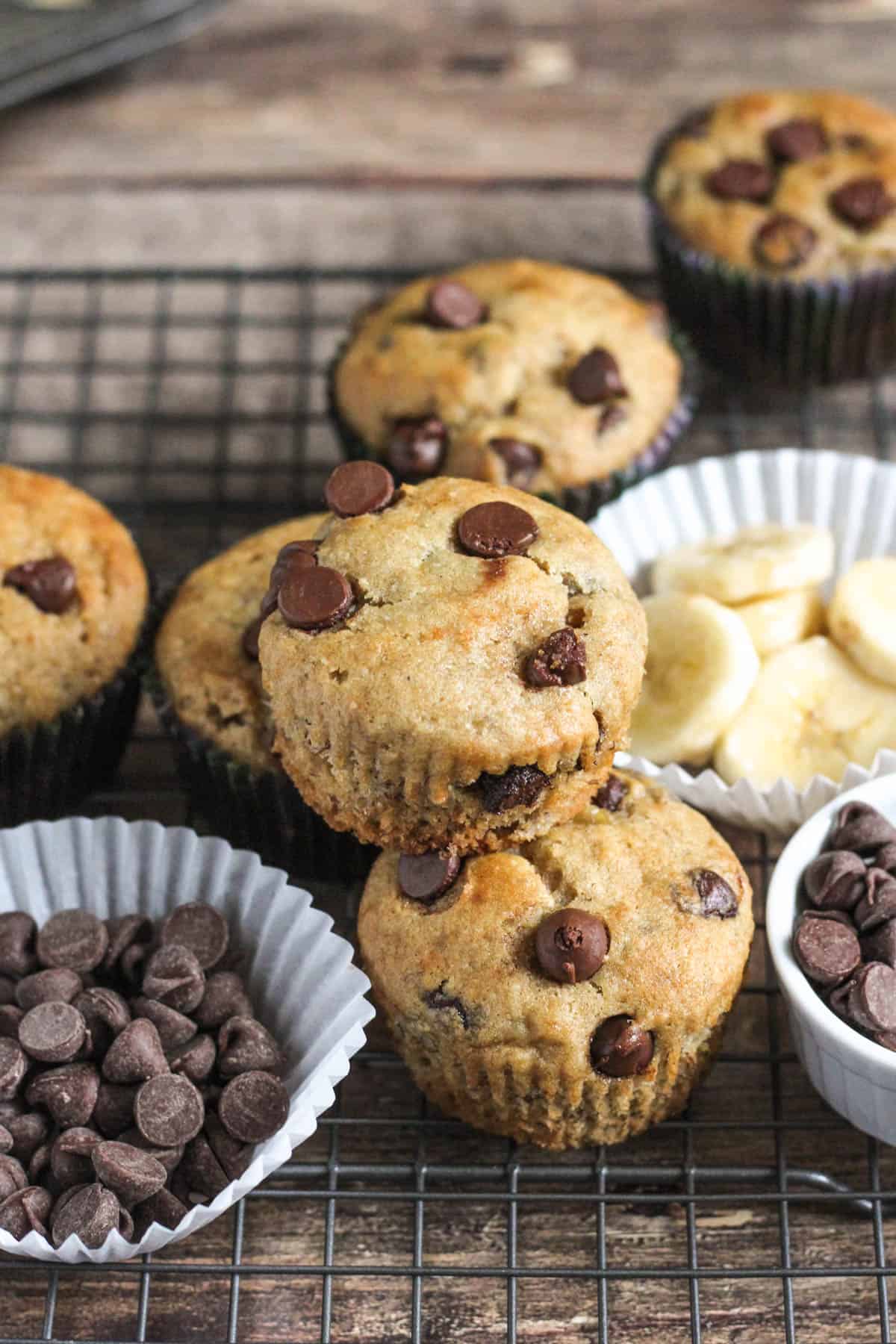 gluten free banana muffins surrounded by muffin liners filled with chocolate chips and bananas with a dark colored background