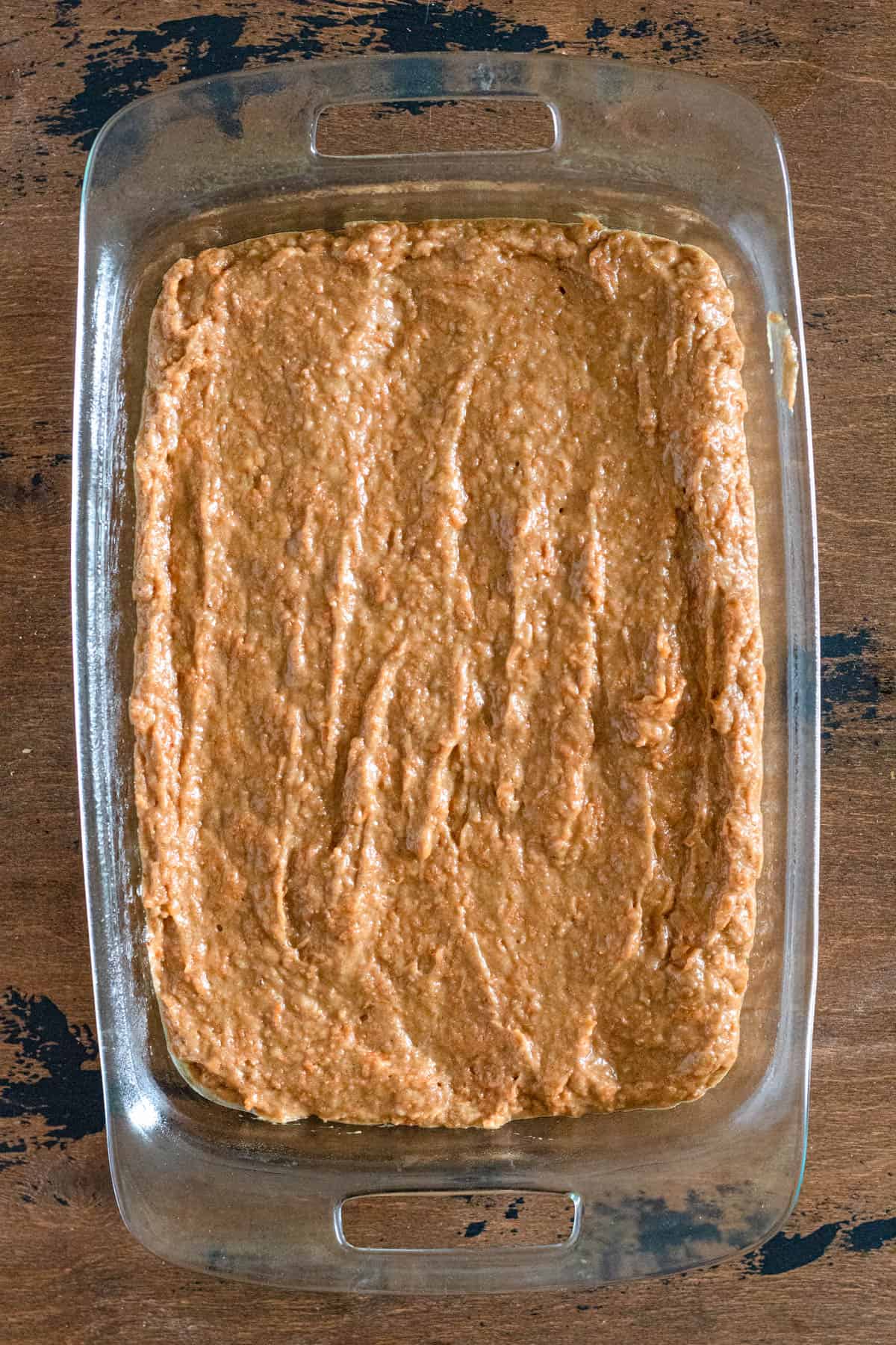 glass baking dish filled with gluten free carrot cake batter with a dark wood colored background