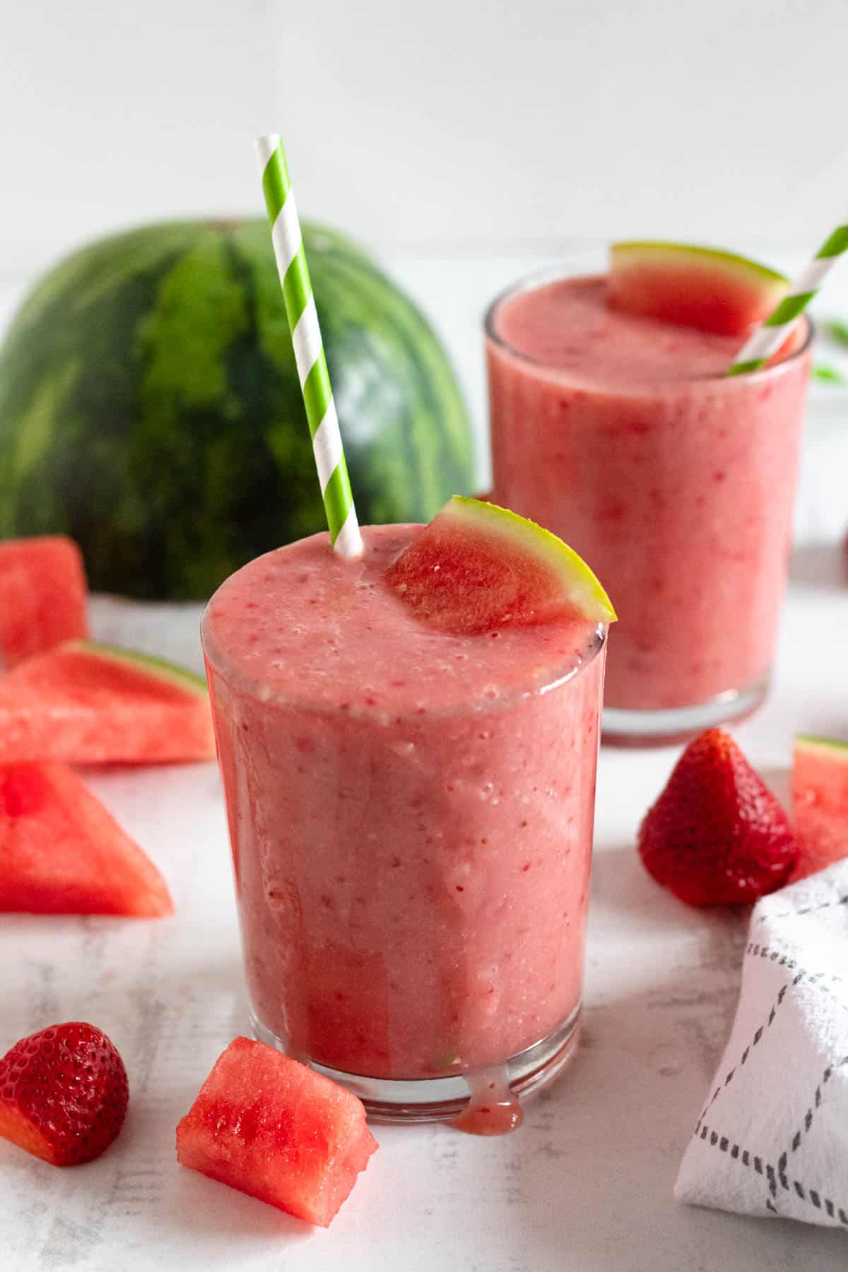 two glasses of easy watermelon smoothie with green and white striped straw with a light background