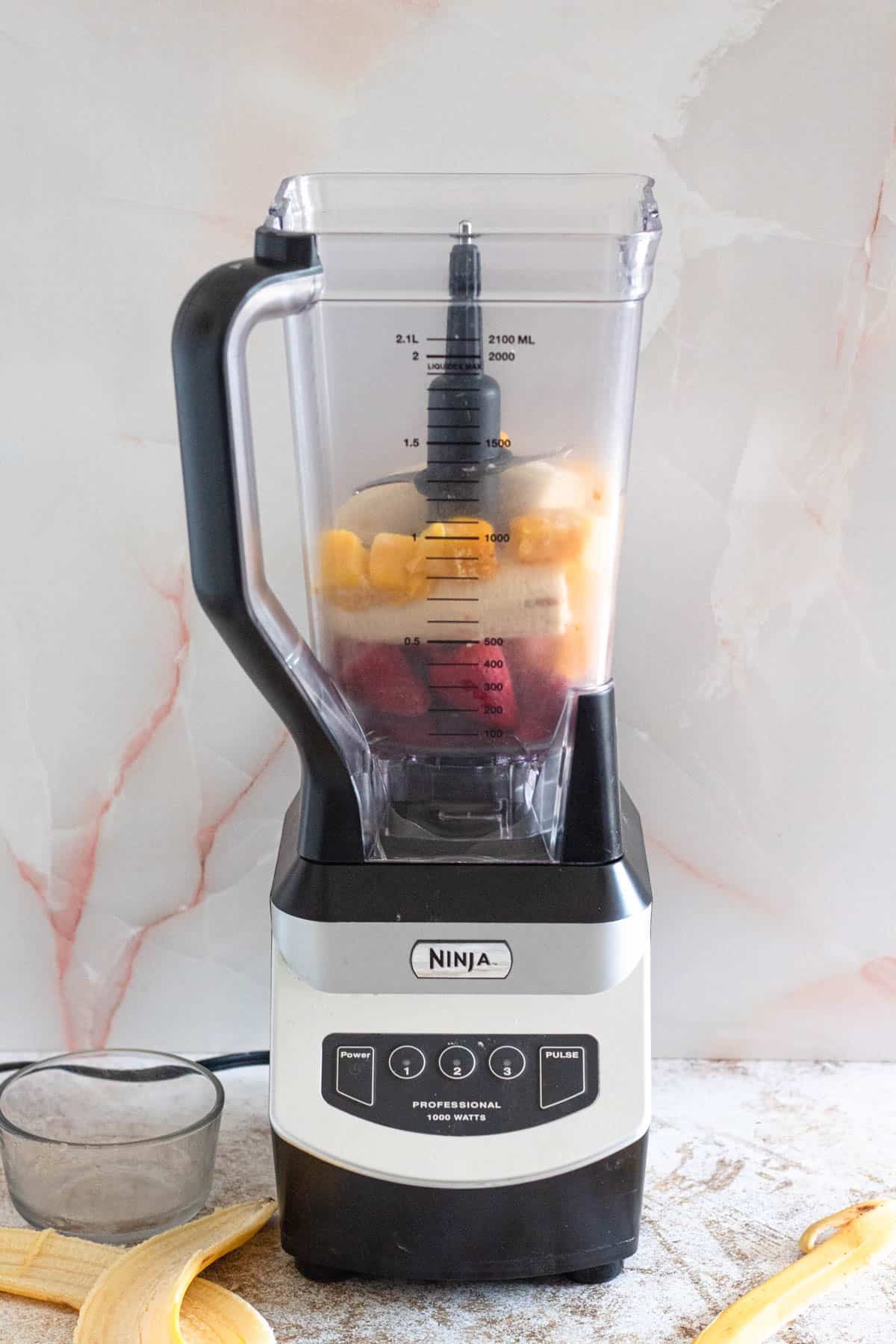 blender with beet smoothie ingredients inside with a light colored background