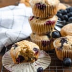 easy gluten free blueberry muffins in front of a small glass bowl of blueberries and a baking towel