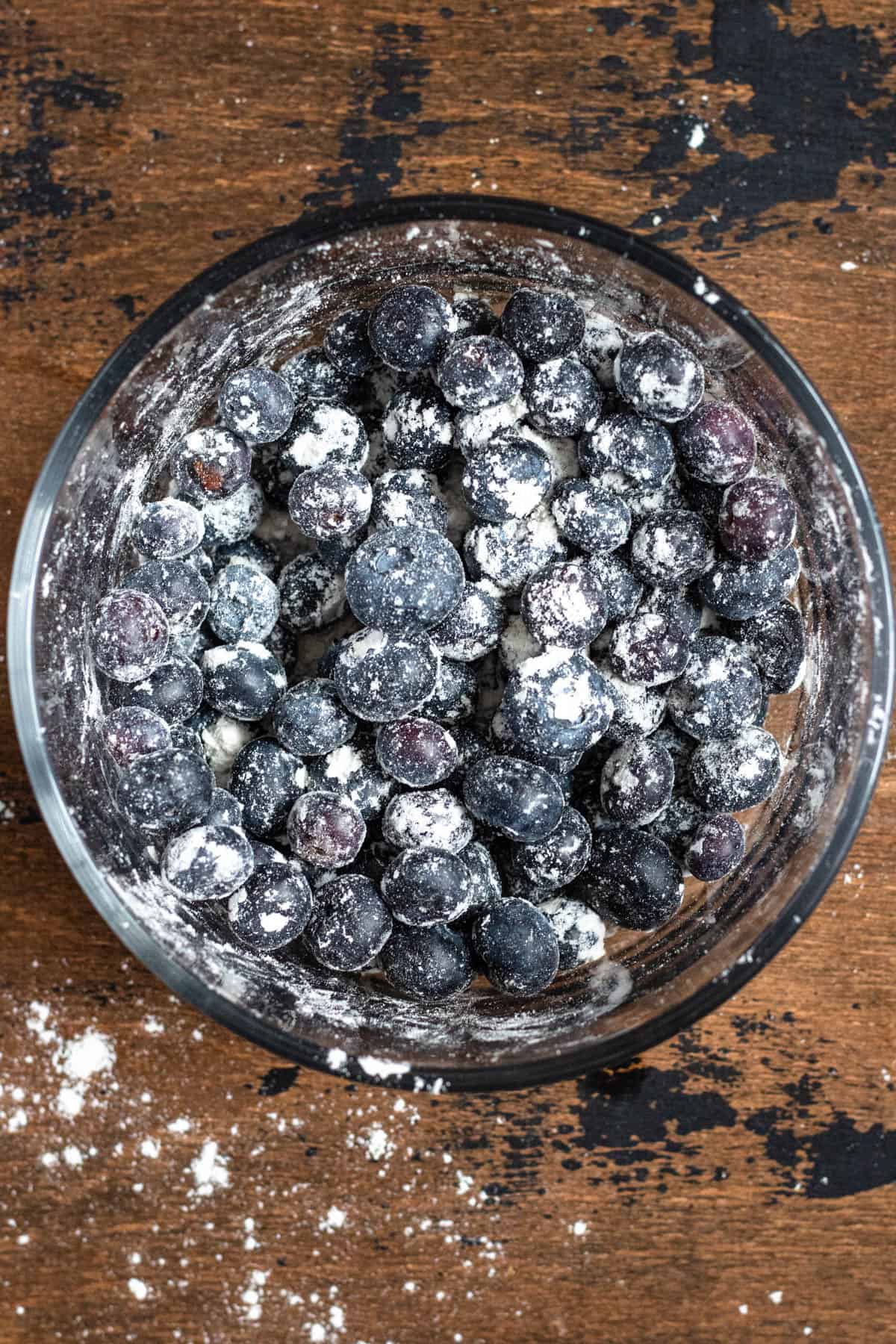 glass bowl filled with fresh blueberries topped with flour with a dark colored background