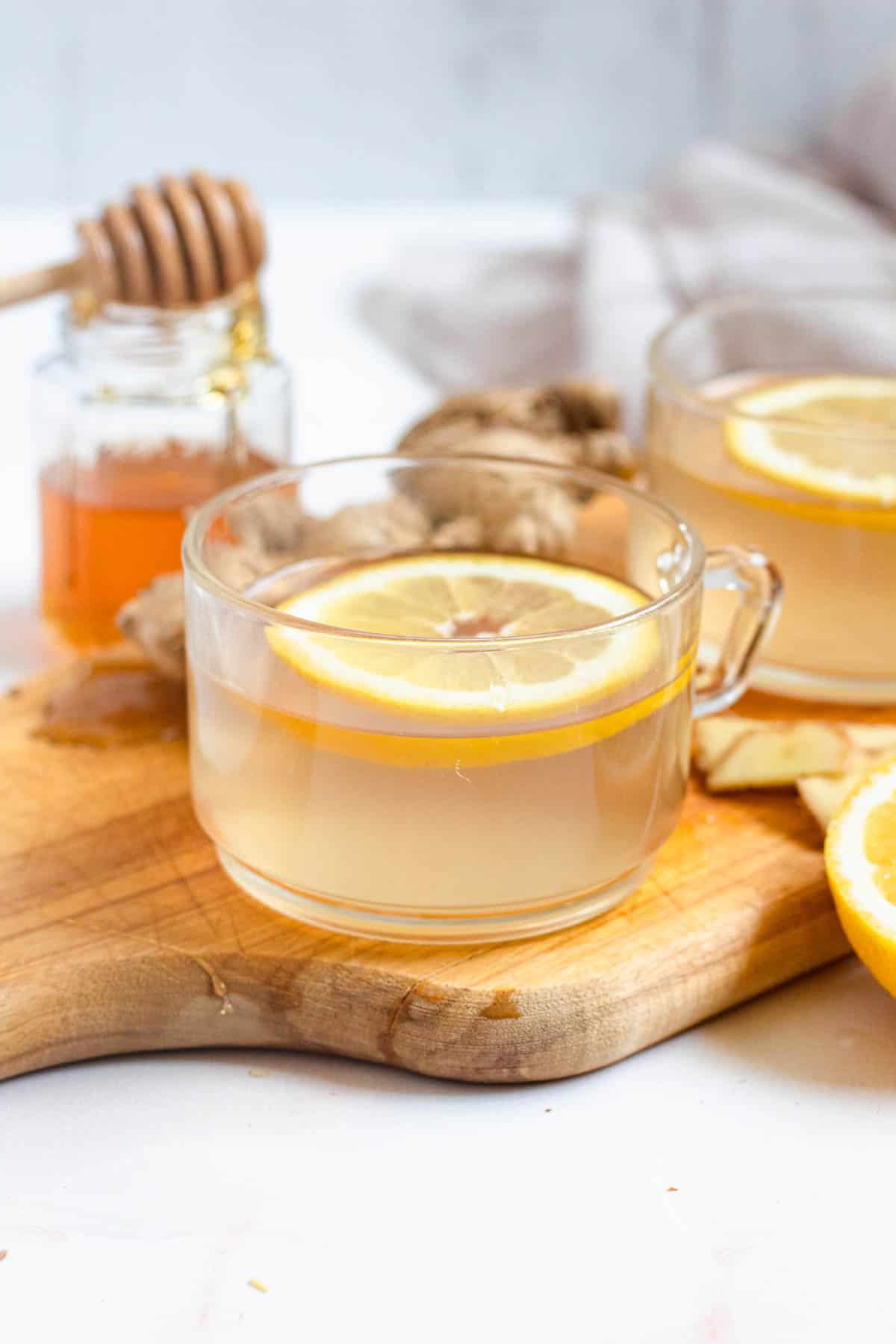 fresh ginger tea in a small glass topped with a sliced lemon with a light colored background