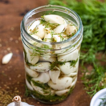 jar of pickled garlic in front of fresh herbs with a dark colored background