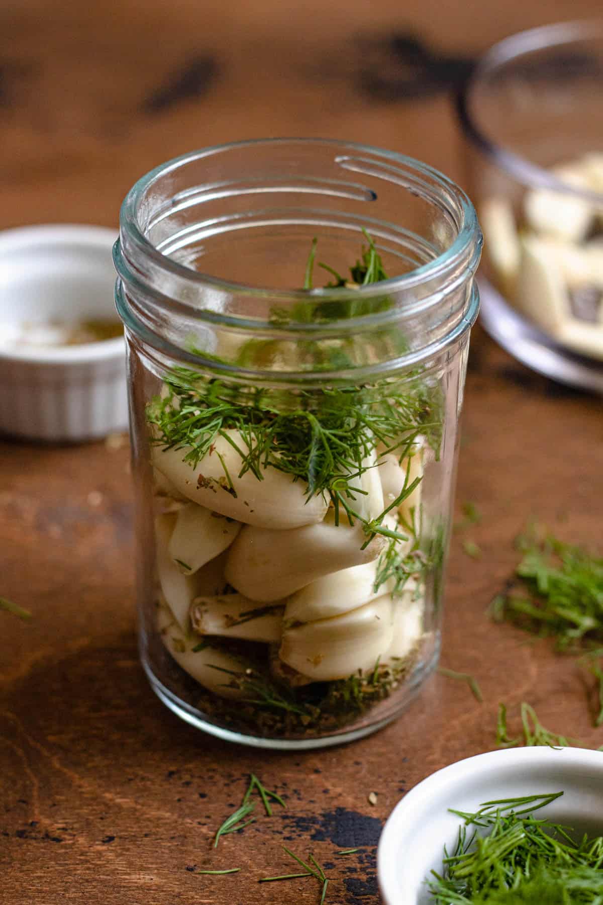 jar of garlic cloves and fresh herbs with a dark colored background