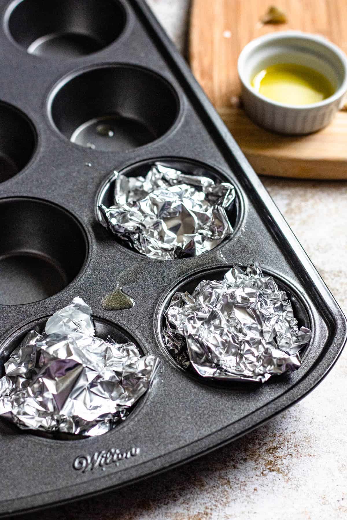 tinfoil covering garlic bulbs in muffin tin