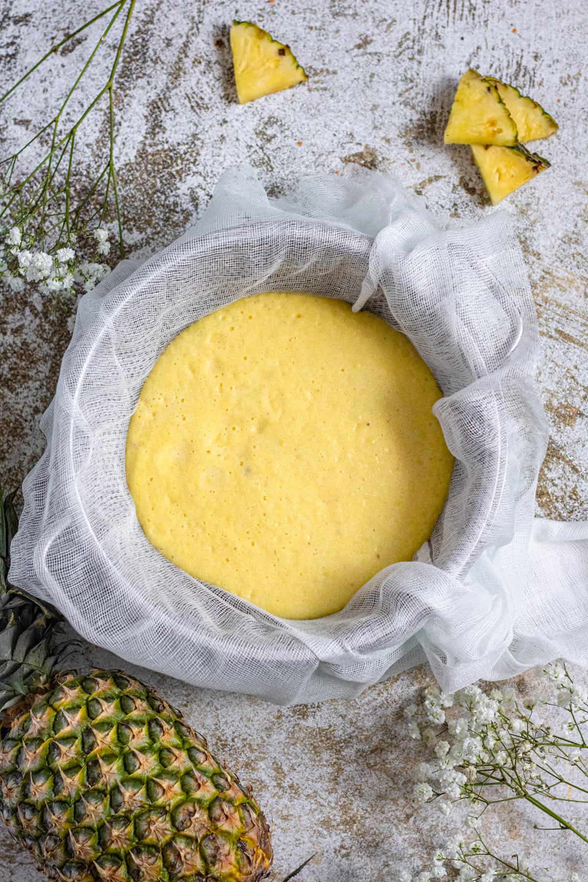 colander with cheesecloth filled with pineapple juice with a light colored background