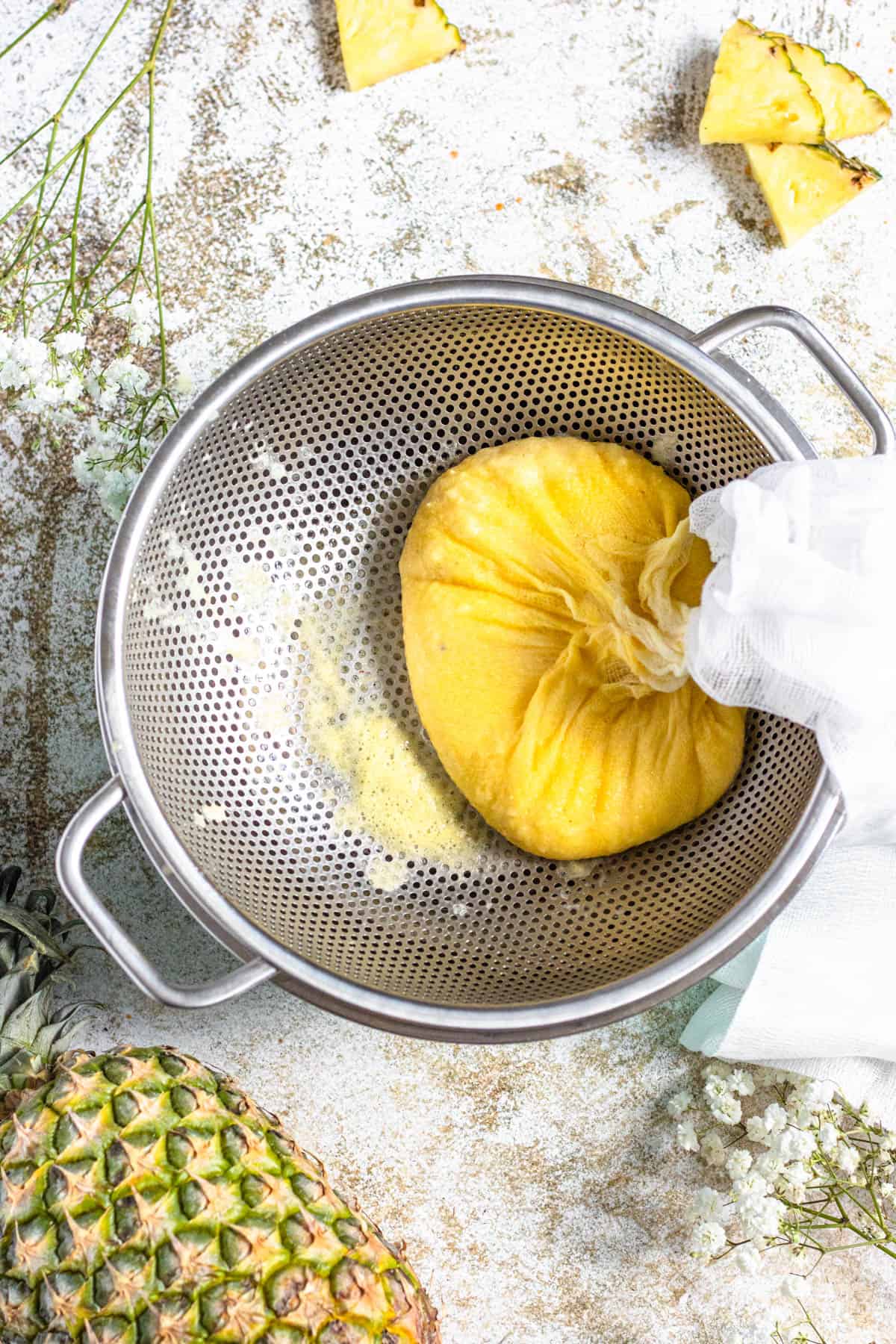 cheesecloth corners pulled together to strain pineapple juice