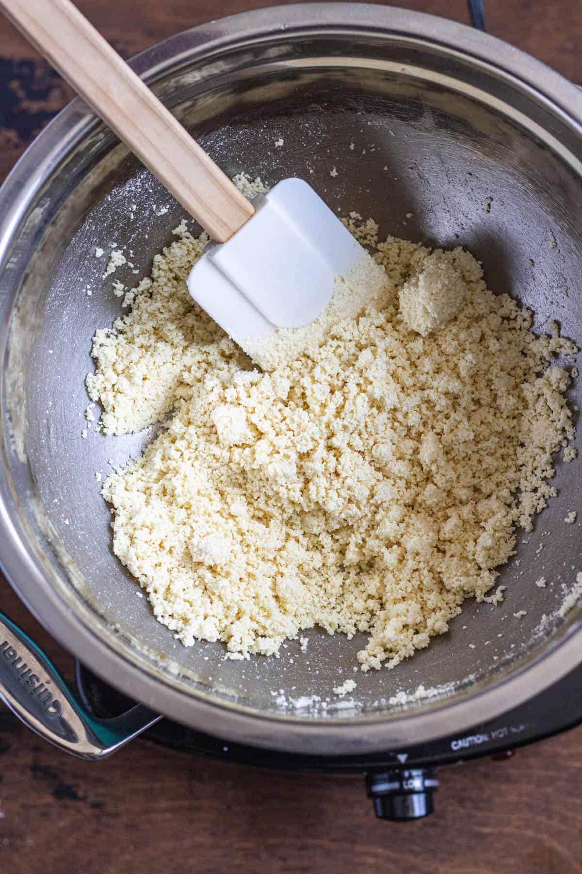 white chocolate recipe ingredients combined and in a crumbly form with a spatula in a metal bowl