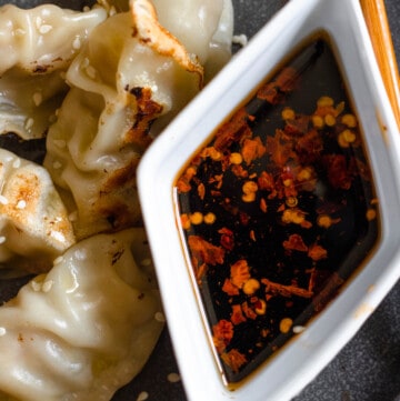 gyoza dipping sauce in a small white diamond dish sitting next to dumplings with a dark colored background