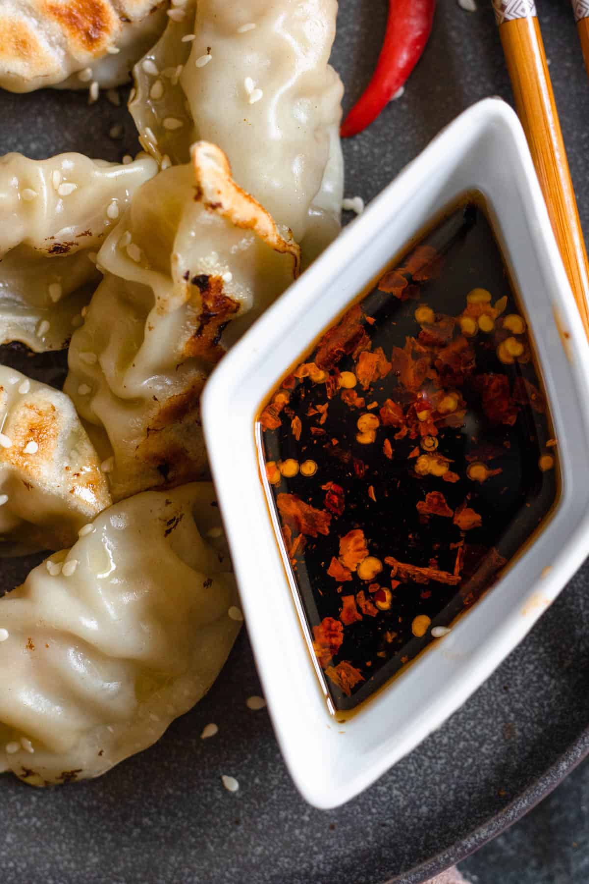gyoza dipping sauce in a small white diamond dish sitting next to dumplings with a dark colored background