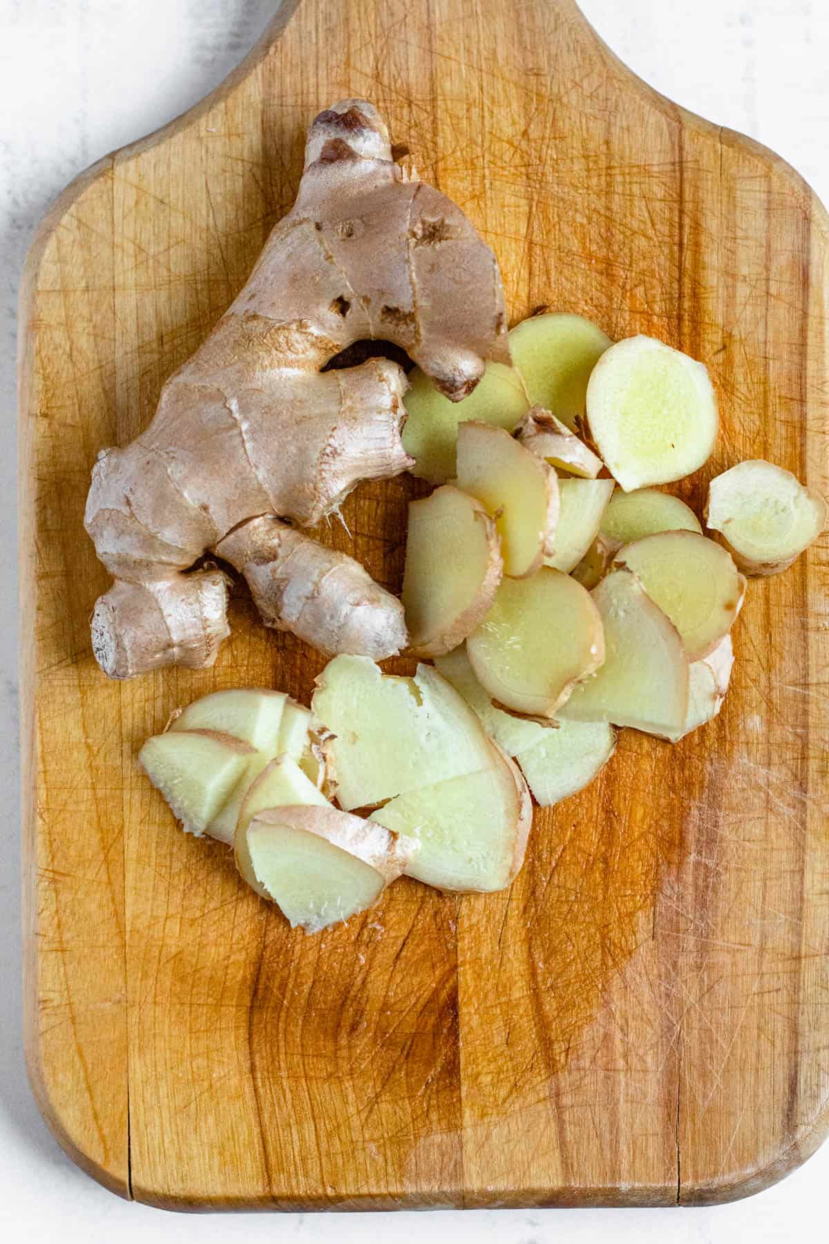 cut up fresh ginger on a wooden cutting board with a light colored background