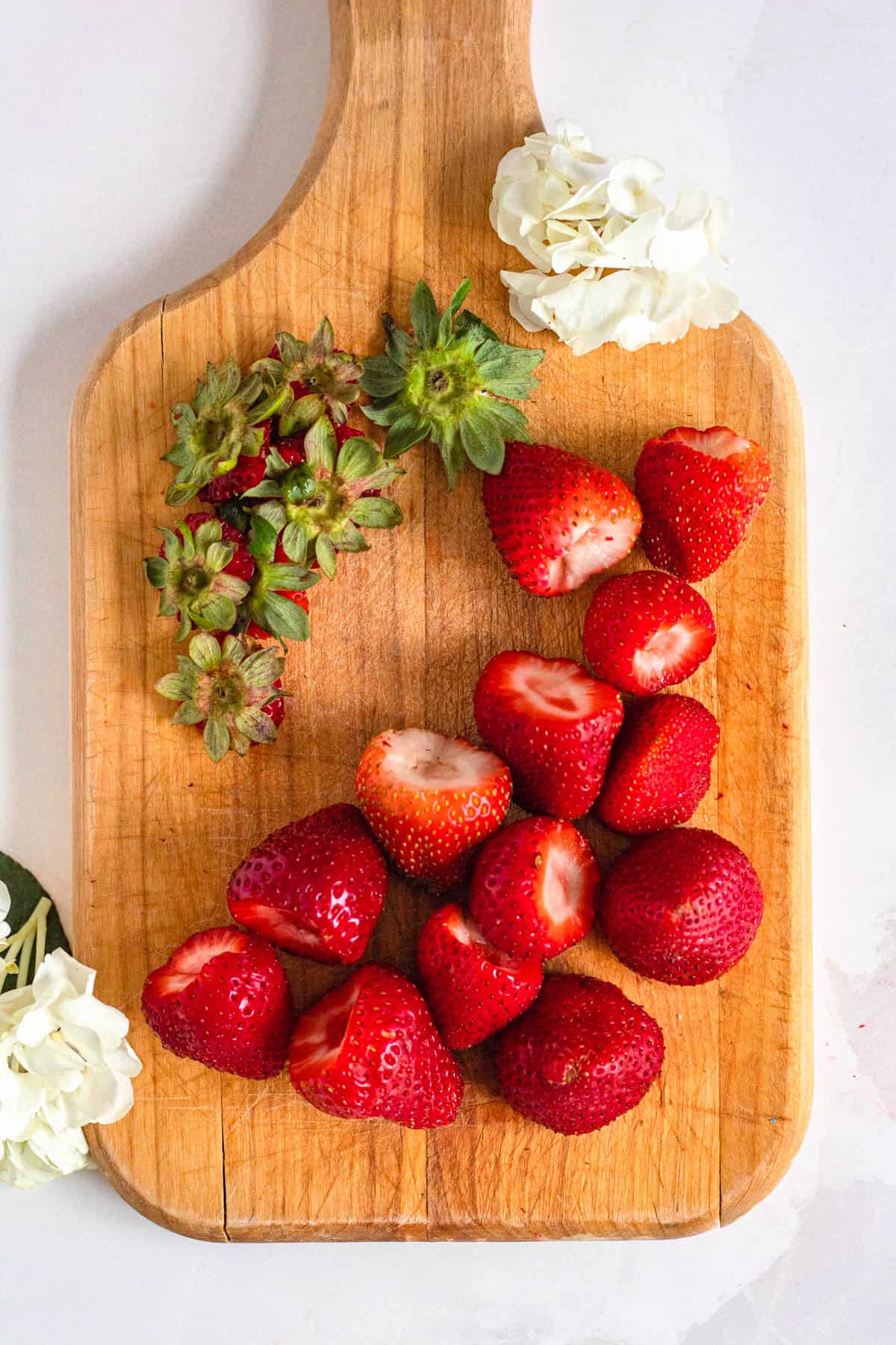 strawberries with the top cut off on a wood cutting board with a light colored background