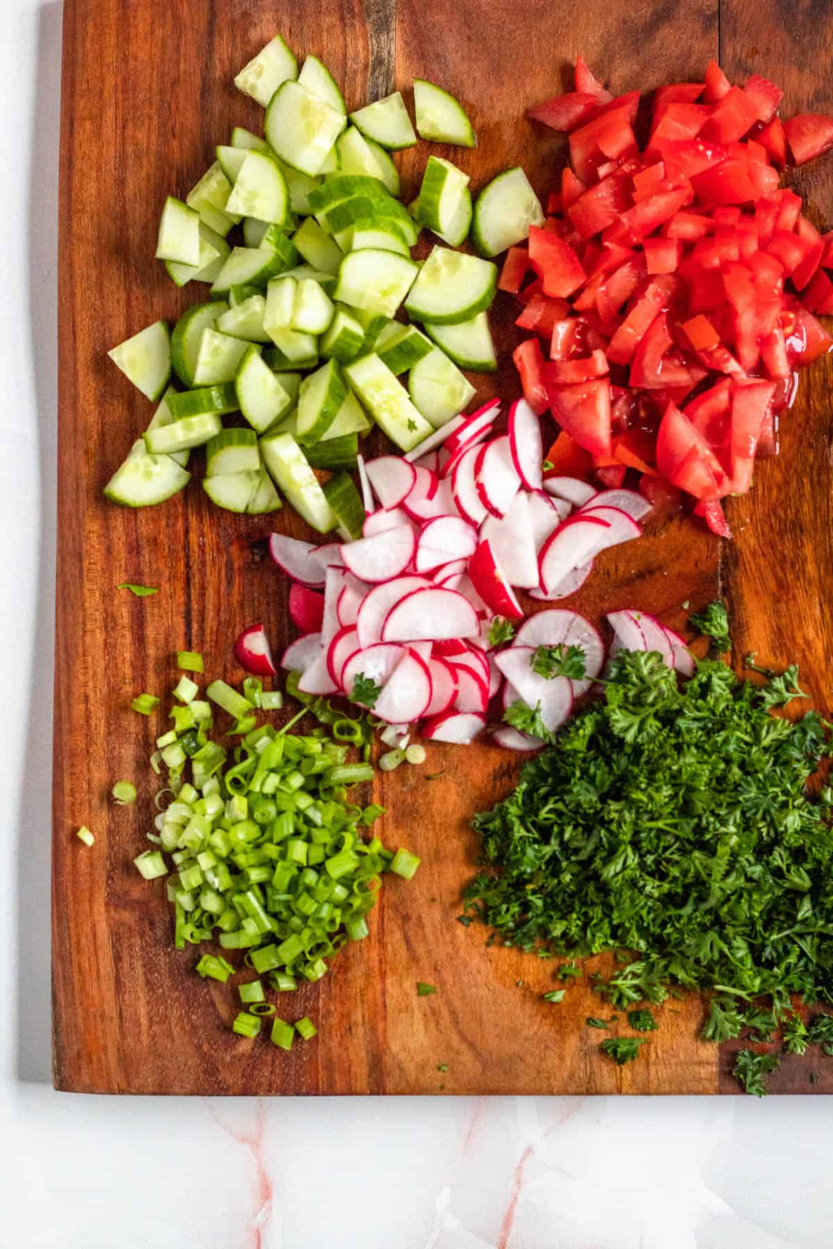 fattoush salad ingredients chopped up on a dark wooden cutting board