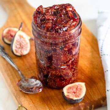homemade fig jam in a mason jar on a wooden cutting board with a light colored background
