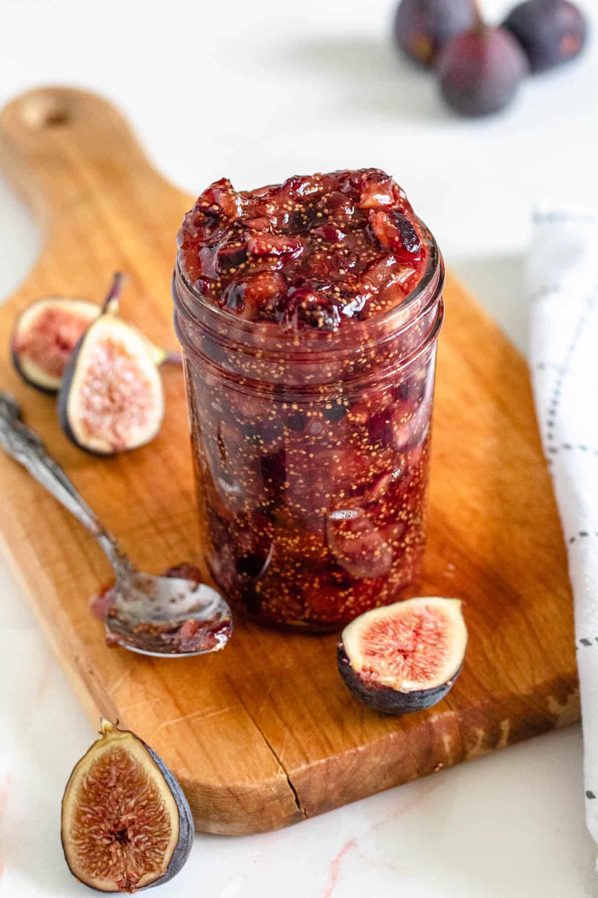 homemade fig jam in a mason jar on a wooden cutting board with a light colored background