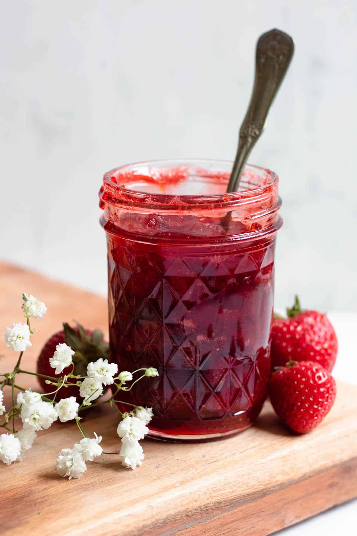 strawberry jam in a mason jar with a spoon in it with a light colored background