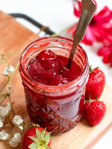homemade strawberry jam in a small glass mason jar with a light colored background