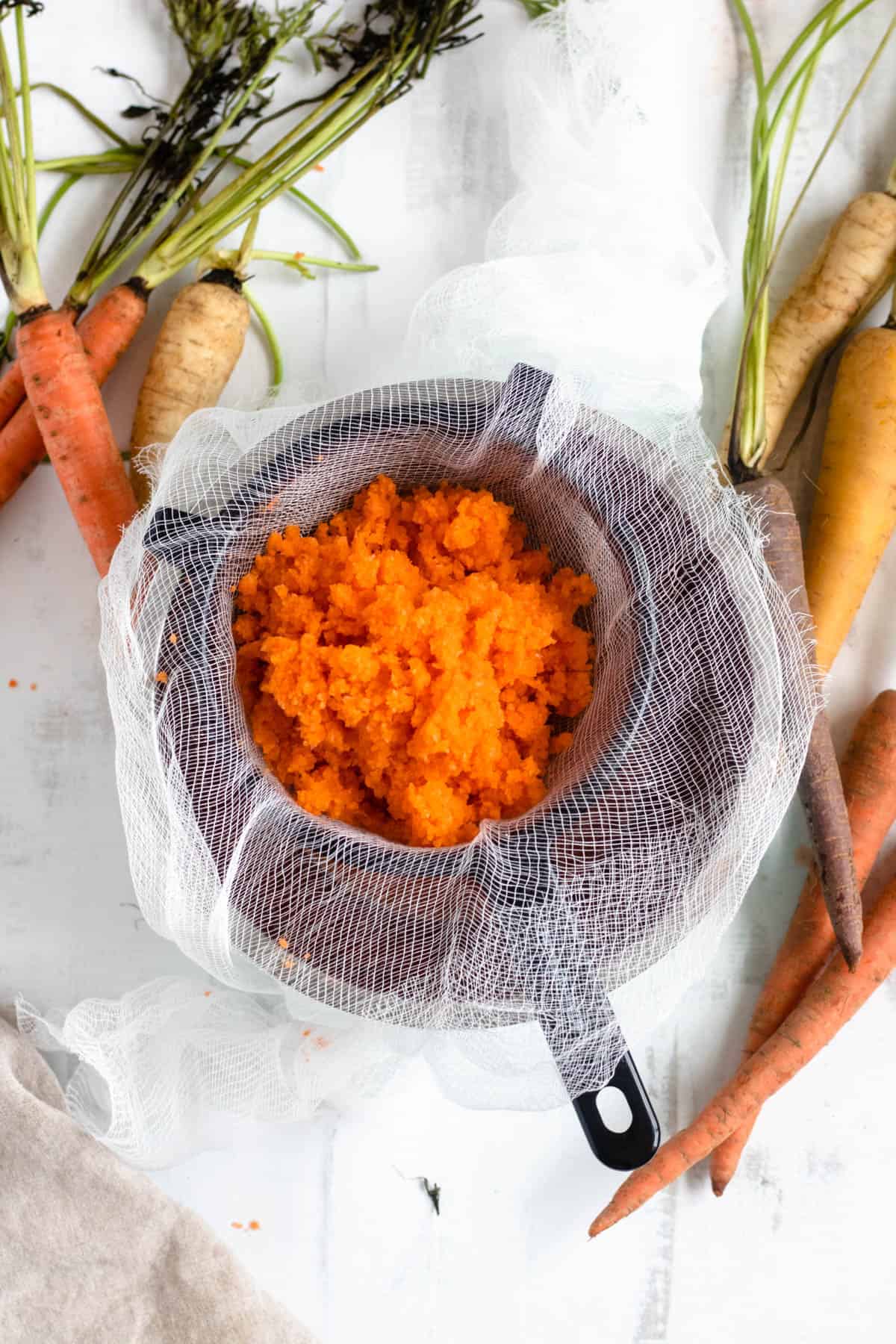 carrot juice being strained through a cheesecloth with a light colored background
