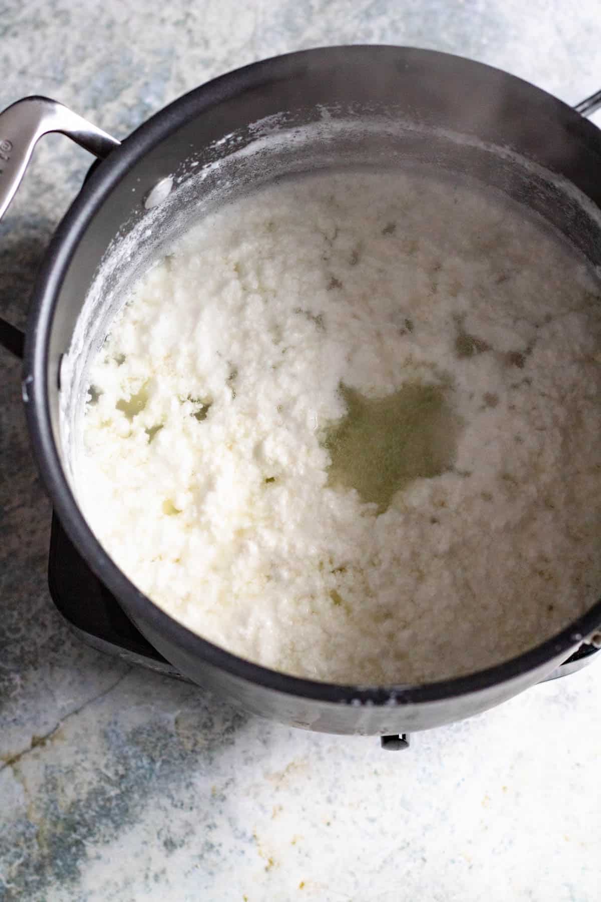 cream cheese in a medium-sized pot with curds at the top 