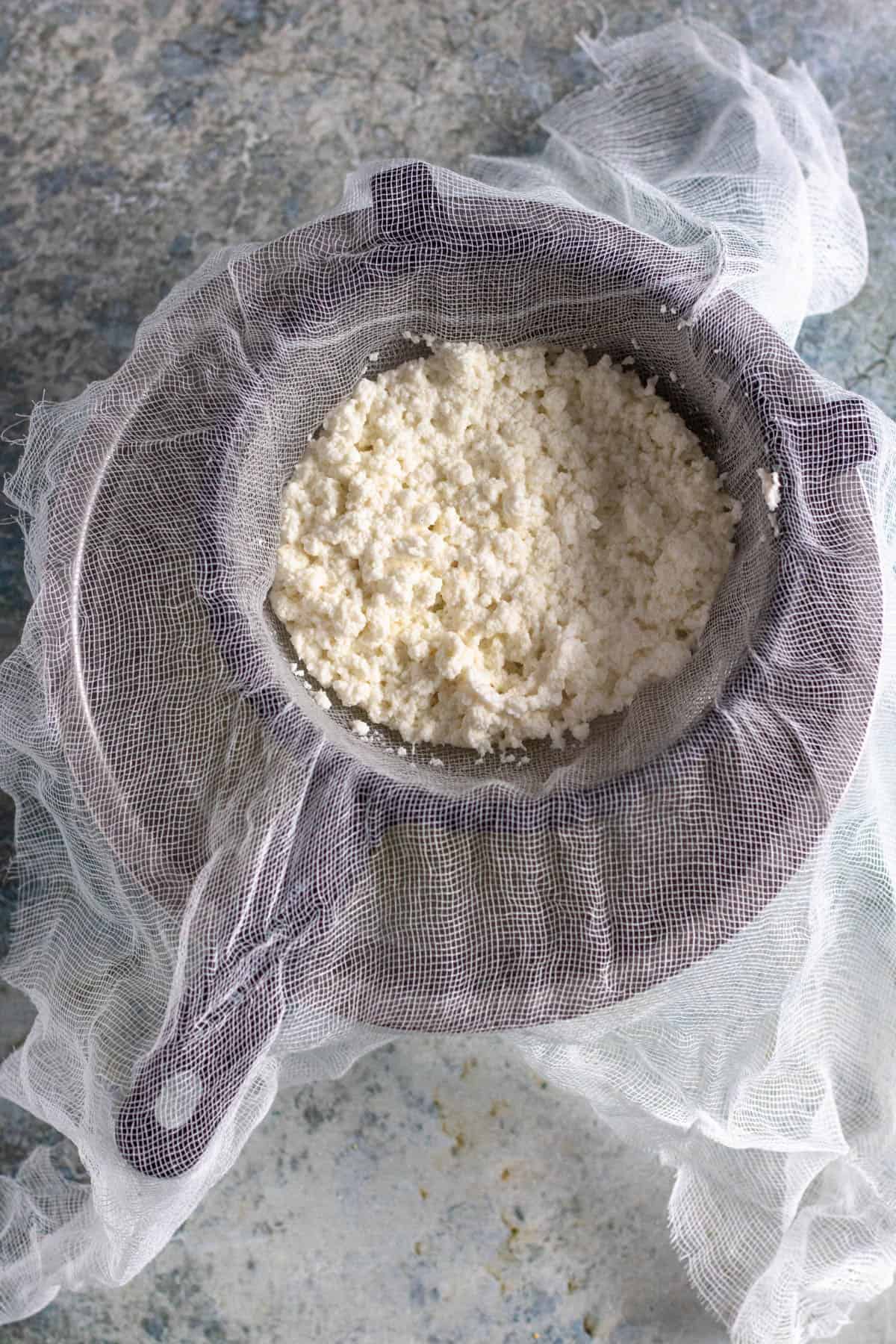 colander lined with a cheesecloth with cream cheese curds 