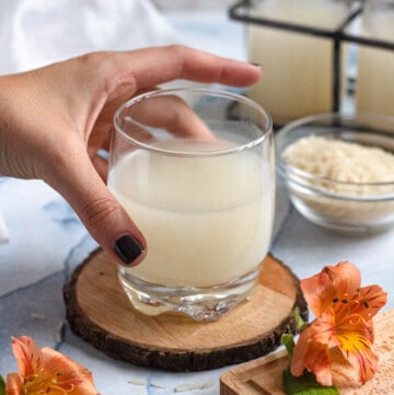 small glass filled with homemade rice milk with a hand holding onto it and a light colored background