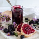 homemade blackberry jam in a glass jar with a light colored background