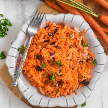carrot and raisin salad in a round glass bowl with a light colored background