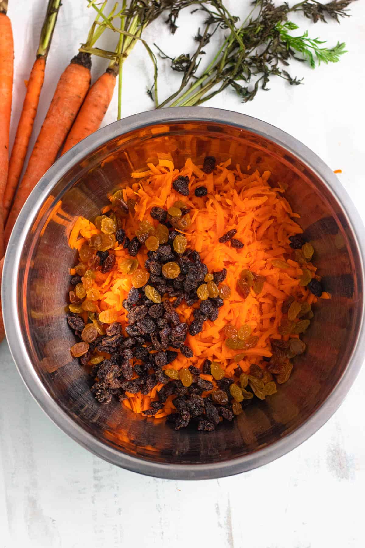shredded carrots with raisins and golden raisins in a bowl with a light colored background 