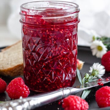 raspberry jam in a glass jar with a light colored background