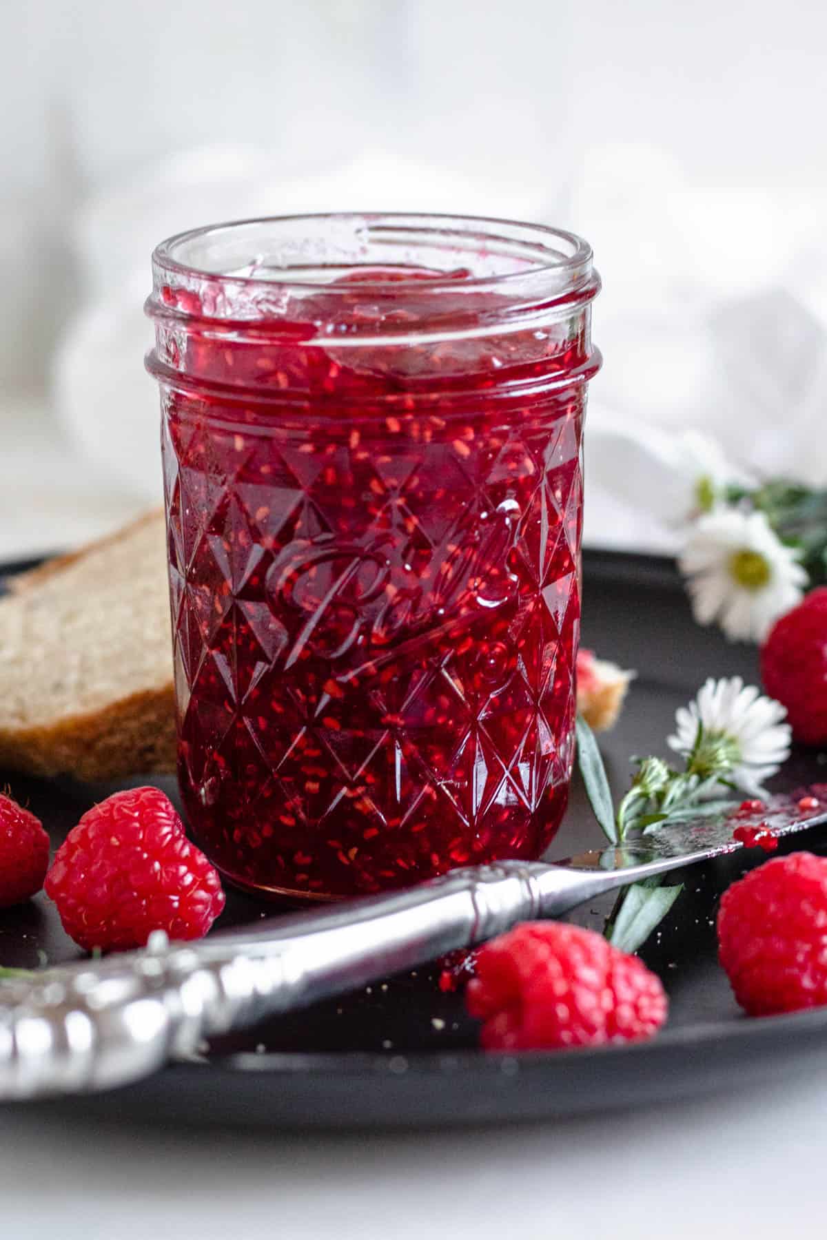 raspberry jam in a glass jar with a light colored background